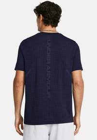 Mørkeblå kortærmet skjorte med et struktureret rutenetmønster. Har Under Armour-logoet lodret langs ryggen. Blødt materiale.