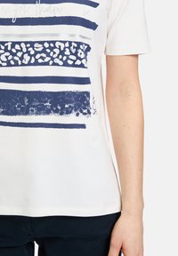 White cotton t-shirt featuring horizontal navy stripes with various textures and a printed graphic. Short sleeves and a round neckline.