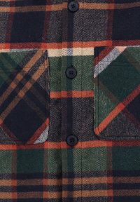 Camicia in flanella a quadri con bottoni neri, con motivi a quadri verdi, rossi e marroni su sfondo blu navy, e due tasche sul petto.
