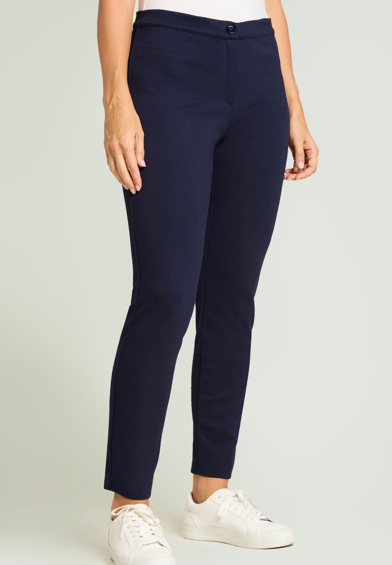 Pantalones entallados de color azul marino con un corte ajustado, que cuentan con cierre de botón, bolsillos delanteros y una textura suave, combinados con zapatillas blancas.