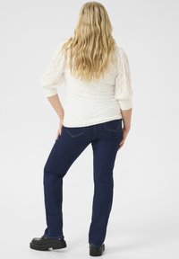 Haut en tricot texturé blanc avec des manches trois-quarts, associé à un jean droit bleu marine et des chaussures à plateforme noires.