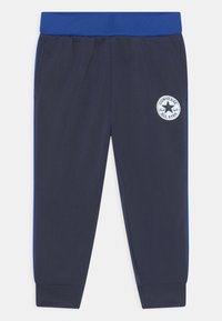 Pantalones de jogging navy con una cinturilla elástica azul, bolsillos laterales y un parche circular blanco con un logo que presenta una estrella y texto.