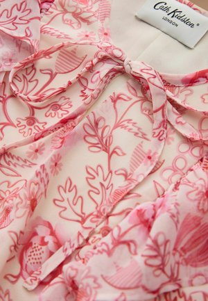 Jasnoróżowa bluzka w czerwone kwiatowe wzory, z kokardą wiązaną przy dekolcie oraz widoczną metką Cath Kidston London.