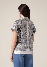 Blusa a maniche corte in tessuto leggero con un intricato motivo paisley bianco e nero, dotata di un colletto discreto e una vestibilità rilassata.