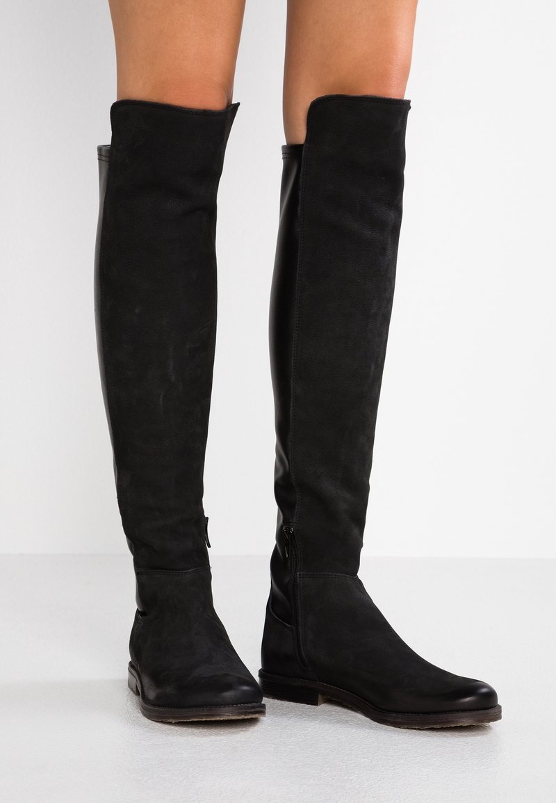 Botas altas negras de muslo, hechas de ante y cuero, con una textura suave, cremalleras laterales y suela plana. Diseño minimalista.