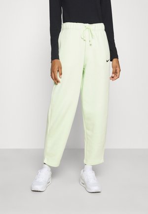 Person wearing light green Nike sweatpants with drawstring waist, black long-sleeve top, white sneakers, standing against a plain background.