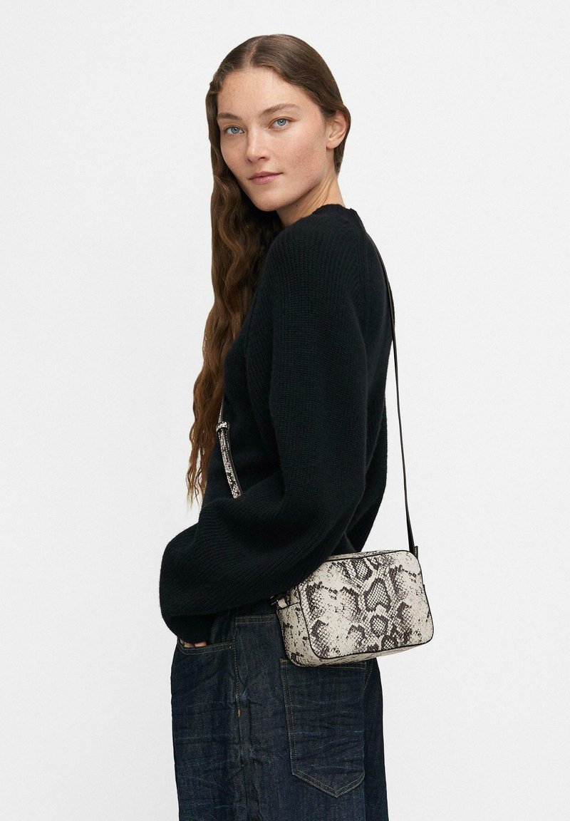 Maglione di cotone nero abbinato a jeans scuri. Borsa a tracolla in stampa pitone bianco e nero con forma rettangolare e tracolla regolabile.