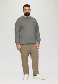 Grijze sweatshirt met ronde hals en geribde manchetten, gecombineerd met beige broek en witte sneakers. Klein logo op de borst van de sweatshirt.