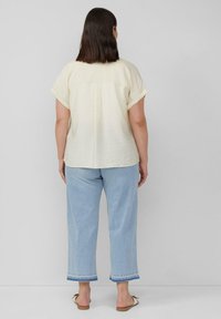 Lichtgele, kortekloof, textuur blouse met een ontspannen pasvorm, gecombineerd met lichtblauwe, wijde jeans met een opgerolde zoom.