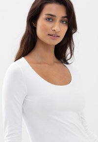 Hvid langærmet bluse med rund halsudskæring, lavet af blødt, glat stof. Tætsiddende design med en minimalistisk stil, ingen synlige mønstre eller detaljer.