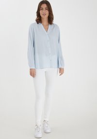 Light blue, long-sleeve button-up shirt with a V-neck and vertical stripes, paired with white skinny jeans and white sneakers.