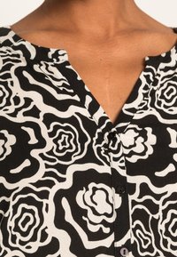 Camicia con motivo floreale in bianco e nero caratterizzata da un scollo a V, dettagli con bottoni e tessuto morbido e leggero.