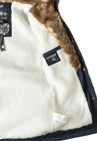 Det isolerade jackans insida har ett mjukt och vitt fuskpälsfoder och en brun pälsdetalj. Inkluderar en marinblå tygetikett med varumärkets logotyp och skötselråd.