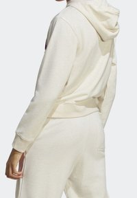 Krämfärgad huvtröja med en texturerad yta, som har passande midja och manschetter, visad bakifrån.