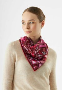 Zijden sjaal met een rood en roze bloemenpatroon, driehoekige vorm, met een zachte textuur en contrasterende rand, gedragen om de nek.