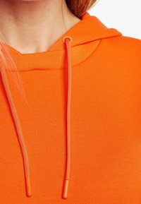 Sudadera naranja con un tejido texturizado, que presenta una capucha con cordón y toggles naranjas a juego, destacando un acabado suave y vibrante.