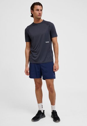 Grå atletisk t-shirt, marineblå shorts, sorte sneakers med hvid logo-detalje. Stoffet ser letvægts og åndbart ud til aktiv brug.