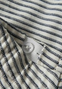 Gros plan sur un tissu tricoté blanc plié avec de fines rayures horizontales gris foncé et un bouton en plastique transparent cousu sur un matériau en maille blanche.