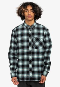 Rutet flannel skjorte i sort, grøn og hvid. Knappet design med en enkelt brystlomme og lange ærmer. Blød tekstur.
