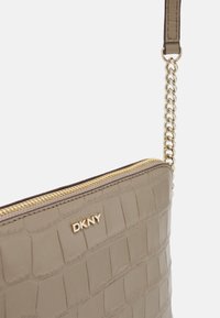 Borsa in ecopelle beige con stampa coccodrillo, zip dorata, tracolla a catena e logo "DKNY" impresso sul davanti.