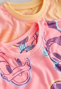 Deux t-shirts en coton empilés, l'un pêche avec une impression de personnage Disney, l'autre rose clair avec un design graphique. Cols ronds mis en valeur.