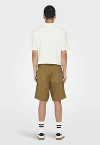 Brune cargo shorts med flere lommer, parret med en lysfarvet kortærmet skjorte. Model iført hvide sokker og sorte sko.