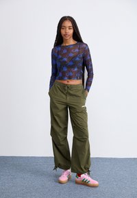 Modra grafična mrežasta majica z dolgimi rokavi, olivno zeleni hlače z vrvico in roza teniske z zelenimi črtami, z ohlapnim krojem in poudarjenimi detajli.