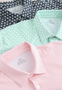 Tri zložené pánske košele so zapínaním na gombíky v regular fit strihu s geometrickými vzormi v námorníckej bielej, zelenej bielej a červenej bielej farbe.