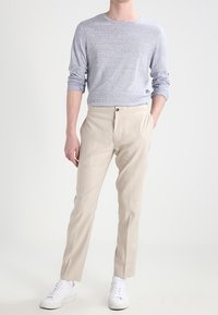 Chemise à manches longues gris clair, pantalon beige sur mesure, baskets blanches, coupe décontractée, tissu texturé, finition lisse, design minimaliste.