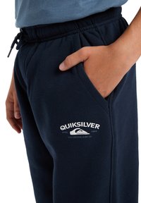 Navyblaue Baumwoll-Sweatpants mit elastischem Bund, Kordelzug und Seitennaht. Mit einem weißen Logo auf dem Oberschenkel.