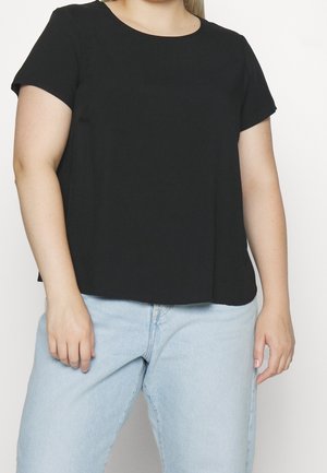 Person wearing plain black short-sleeve shirt and light blue jeans against a white background, shown from neck to hips.