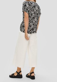 Top de manga corta con estampado de paisley en blanco y negro, combinado con pantalones de pierna ancha blancos y sandalias planas negras con tiras.