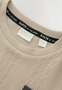 Béžové bavlnené tričko s textúrovaným tkaným vzorom, okrúhlym výstrihom, s etiketami "BAKER by Ted Baker" a "Vyrobené v Turecku", s čiernym lemovaním.