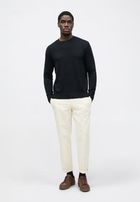Pulover negru cu guler rotund, pantaloni crema tapered și adidași maro. Design simplu cu o textură netedă și manșete răsucite la pantaloni.