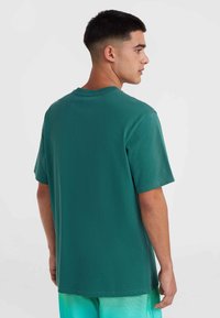 Camiseta de manga corta en color verde azulado con cuello redondo y corte relajado. Textura de algodón suave, diseño sencillo sin patrones ni gráficos visibles.