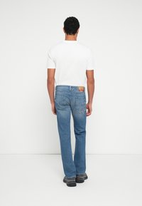 Modre jeans hlače iz jeansa z ravnim krojem nog, nošene z belim majico. Pomembne značilnosti vključujejo zadnje žepe in etiketo na pasu.