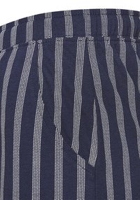 Marinblått tyg med vertikala vita ränder; har elastisk midja och sidoficka; slät textur och lätt design.