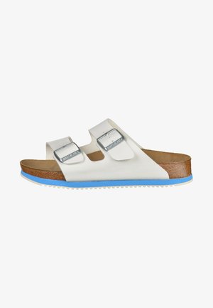 White two-strap sandal with silver buckles, brown cork footbed, and blue rubber outsole; textured soles for traction.