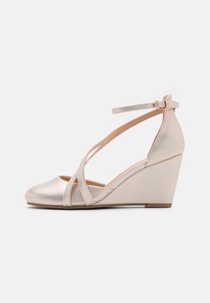 Chaussure compensée en métal beige avec bout fermé, sangles croisées, une bride à la cheville avec boucle dorée, et un talon compensé élevé.