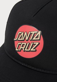 Black cap with a rounded visor, featuring a prominent red circular logo that reads "SANTA CRUZ" in bold, stylized gold text.