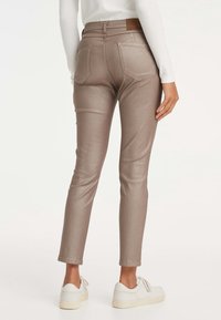 Jean skinny bronze métallisé avec poches arrière et taille mi-haute. Associé à des baskets blanches, présentant une texture lisse et brillante.