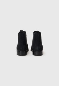 Botas chelsea de ante negro con paneles laterales elásticos y tiradores. Punta redondeada y suelas de goma suave. Diseño minimalista sin patrones visibles.