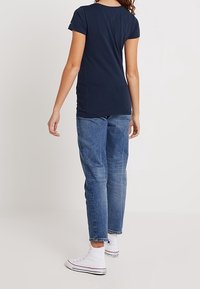 Marinblå kortärmad t-shirt i kombination med ljusblå jeans och vita högklackade sneakers; enkel design med en åtsittande silhuett.