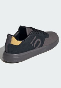 Czarne zamszowe i materiałowe sneakersy z teksturowanym szarym noskiem i żółtym akcentem na pięcie, z czarnymi sznurowadłami i wytłoczonym logo na boku.