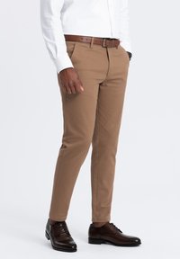 Pantaloni chinos marroni con una finitura testurizzata e una vestibilità su misura, abbinati a una cintura in pelle marrone e scarpe eleganti marroni scuri. Camicia bianca a maniche lunghe.