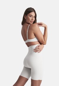 Mameluco blanco sin costuras con tirantes delgados ajustables y cintura alta, que presenta una textura suave y un ajuste ceñido al cuerpo.
