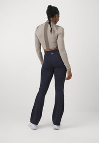 Beige pitkähihaine crop-top, jossa on takana muotoilu, yhdistettynä tummansinisiin leveälahkeisiin housuihin. Sileä pinta, tiukka ja joustava materiaali.