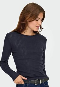 Marinblå långärmad topp med en strukturerad ribbad design. Rund halsringning och figurnära passform, i kombination med denim och ett svart bälte.