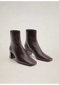 Par de botas de tobillo de cuero marrón oscuro con puntas cuadradas y tacones bajos en un fondo neutral claro.