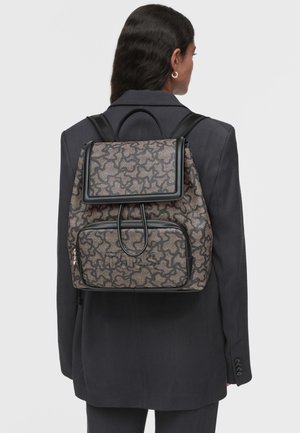 Sac à dos en tissu à motifs, gris et noir, avec une fermeture à rabat et une poche zippée à l'avant. Bretelles réglables et accents lisses.